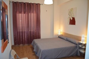 Un dormitorio con cama, una silla, un escritorio, una lámpara y un cuadro en la pared.