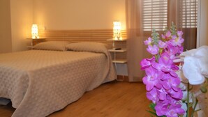 A bedroom with a bed, bedside tables, and a nightstand. There is a window with blinds and a flower arrangement on the nightstand. - Hotel Rural Luna Llena (Torremocha de Jarama)