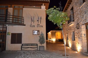 Un edificio llamado Luna Elena con fachada de piedra, un banco y un árbol en el patio.