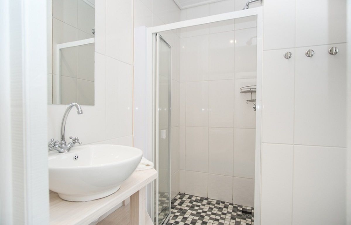 A bathroom with a white sink, a mirror, and a shower area with tiled walls and a checkered floor.