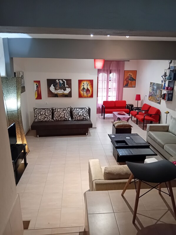 A living room with a sofa, red chairs, a coffee table, and artwork on the walls. - Maisonette Maria - for tranquility. Sykia Chalkidikis (Sithonia)