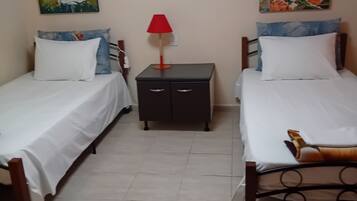 A room with two single beds, a nightstand, a red lamp, and two wall paintings.