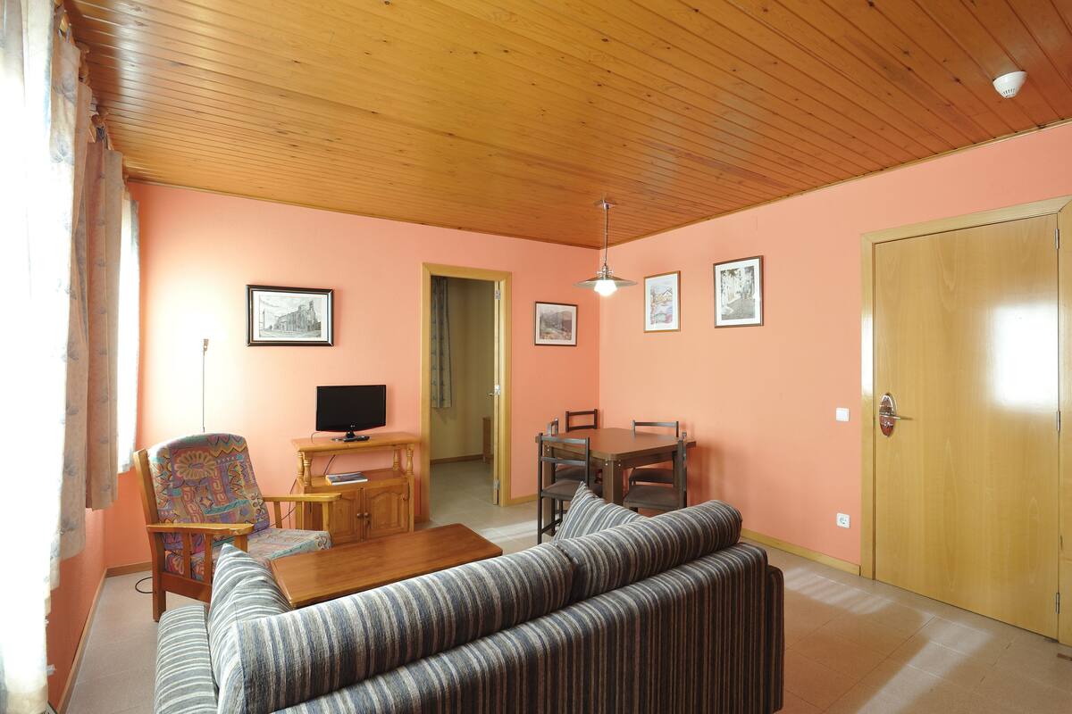 A living room with a wooden ceiling, a sofa, a chair, a table, and a television.