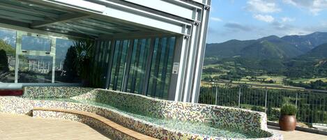 A modern outdoor seating area with a mosaic-tiled bench, a potted plant, and a view of a mountainous landscape.