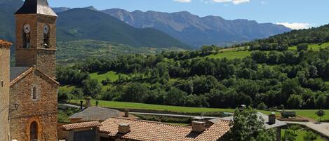 A stone church with a bell tower, surrounded by lush green hills and mountains.