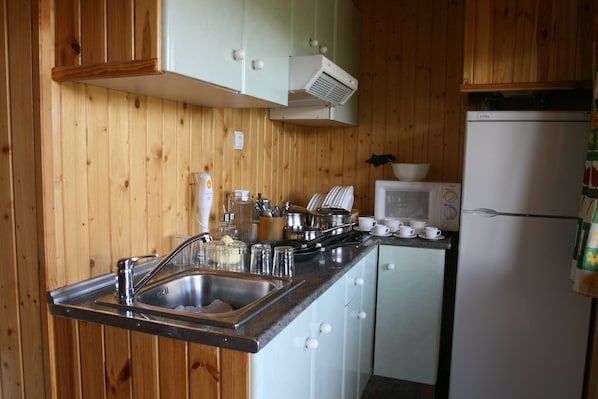 Una cocina con paredes de madera, un lavamanos de acero inoxidable, un microondas y un refrigerador.