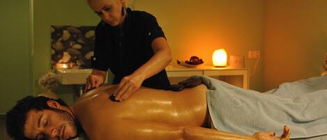 A person receiving a massage in a room with a massage table, a small table with a candle, and a wall decoration.