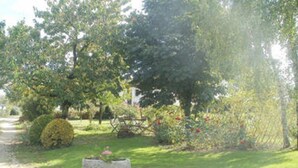 A garden with a stone planter, a wooden bench, and a variety of plants and flowers. - Gite La Raymondiere (Vernoux-en-Gatine)
