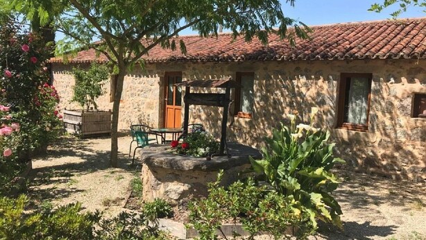 A rustic stone building with a tiled roof, a wooden bench, and a garden with various plants and flowers. - Gite La Raymondiere (Vernoux-en-Gatine)
