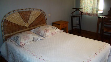 Une chambre à coucher avec un lit, une table de chevet en bois, une chaise et une fenêtre ornée de rideaux à motifs floraux.