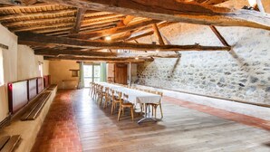 A long dining table with chairs in a rustic room with exposed wooden beams and stone walls. - Gite La Raymondiere (Vernoux-en-Gatine)
