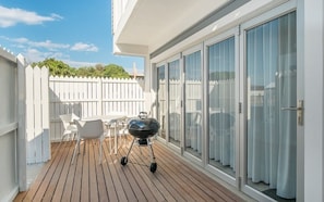 A balcony with a wooden deck, a barbecue grill, and a white fence.