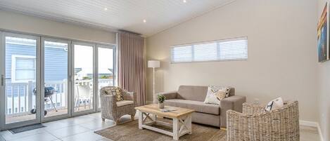A spacious living room with a sliding glass door leading to a balcony, a beige sofa, a coffee table, and wicker furniture.