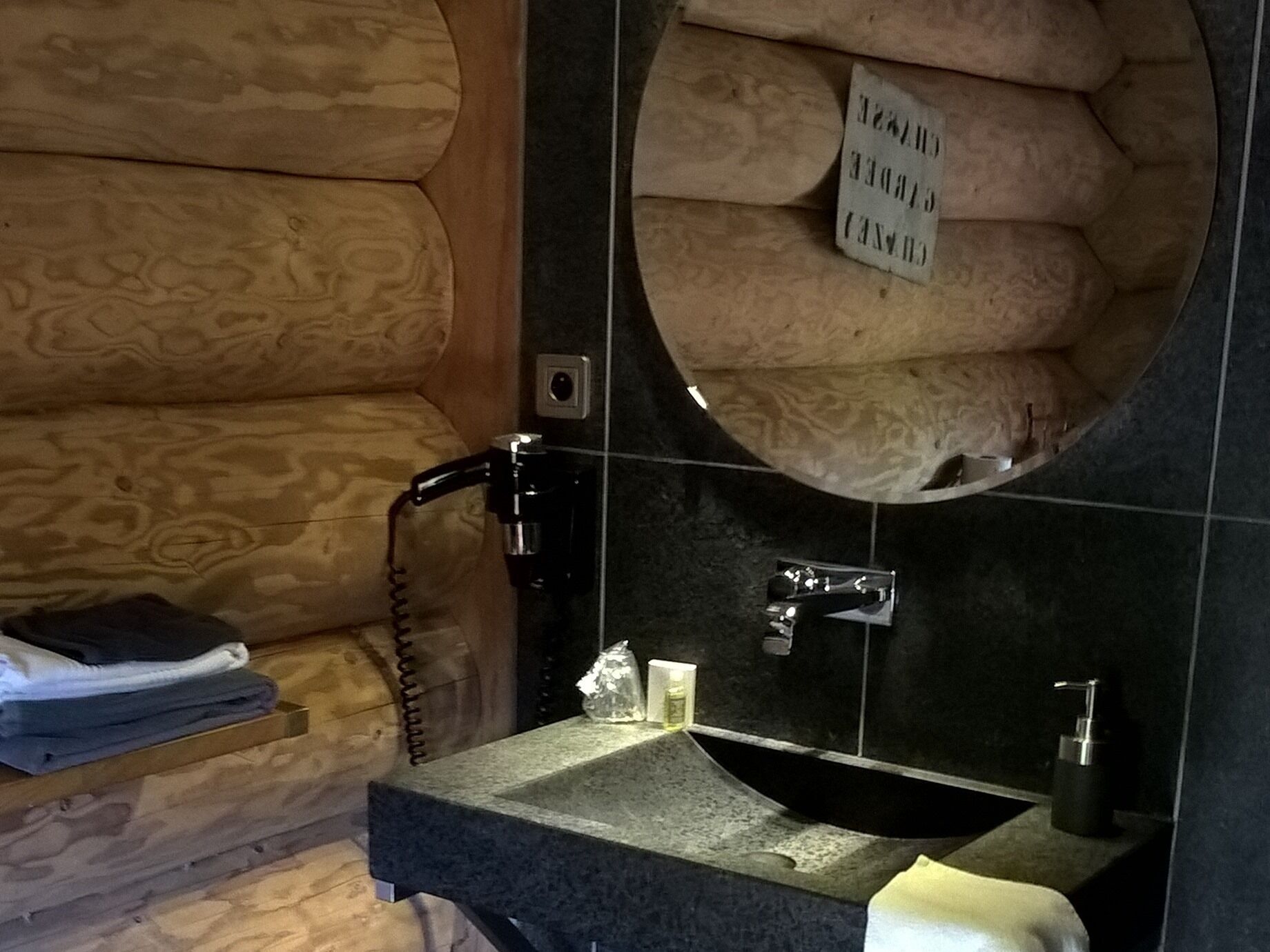 Een badkamer met een houten wand, een ronde spiegel en een wastafel met een kraan.