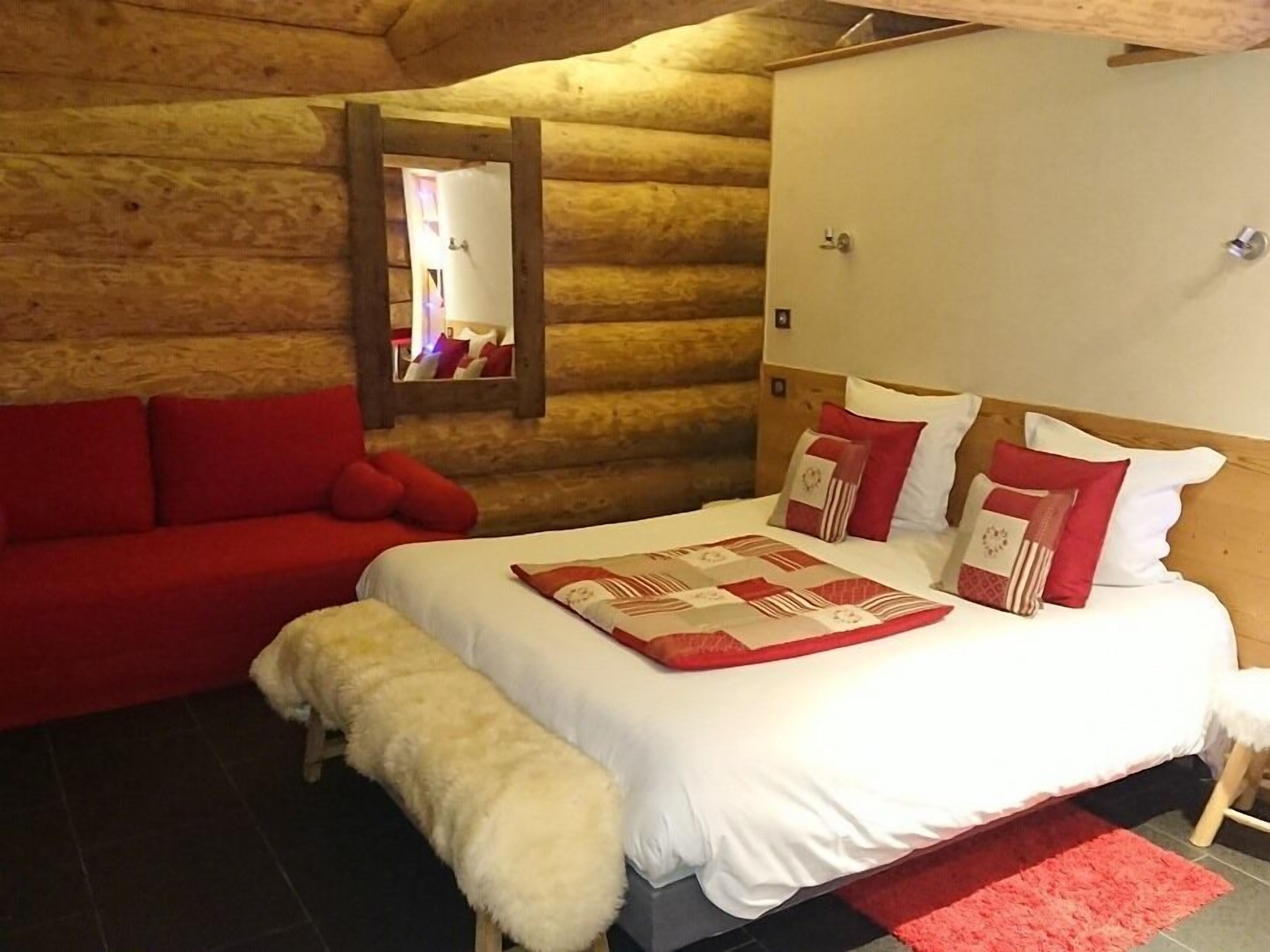 Un dormitorio de estilo cabaña de madera con una cama, un sofá rojo y un banco.