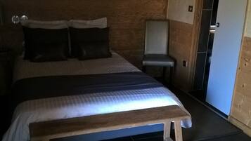 Een slaapkamer met een bed, kussens, een bankje, een stoel en een deur.