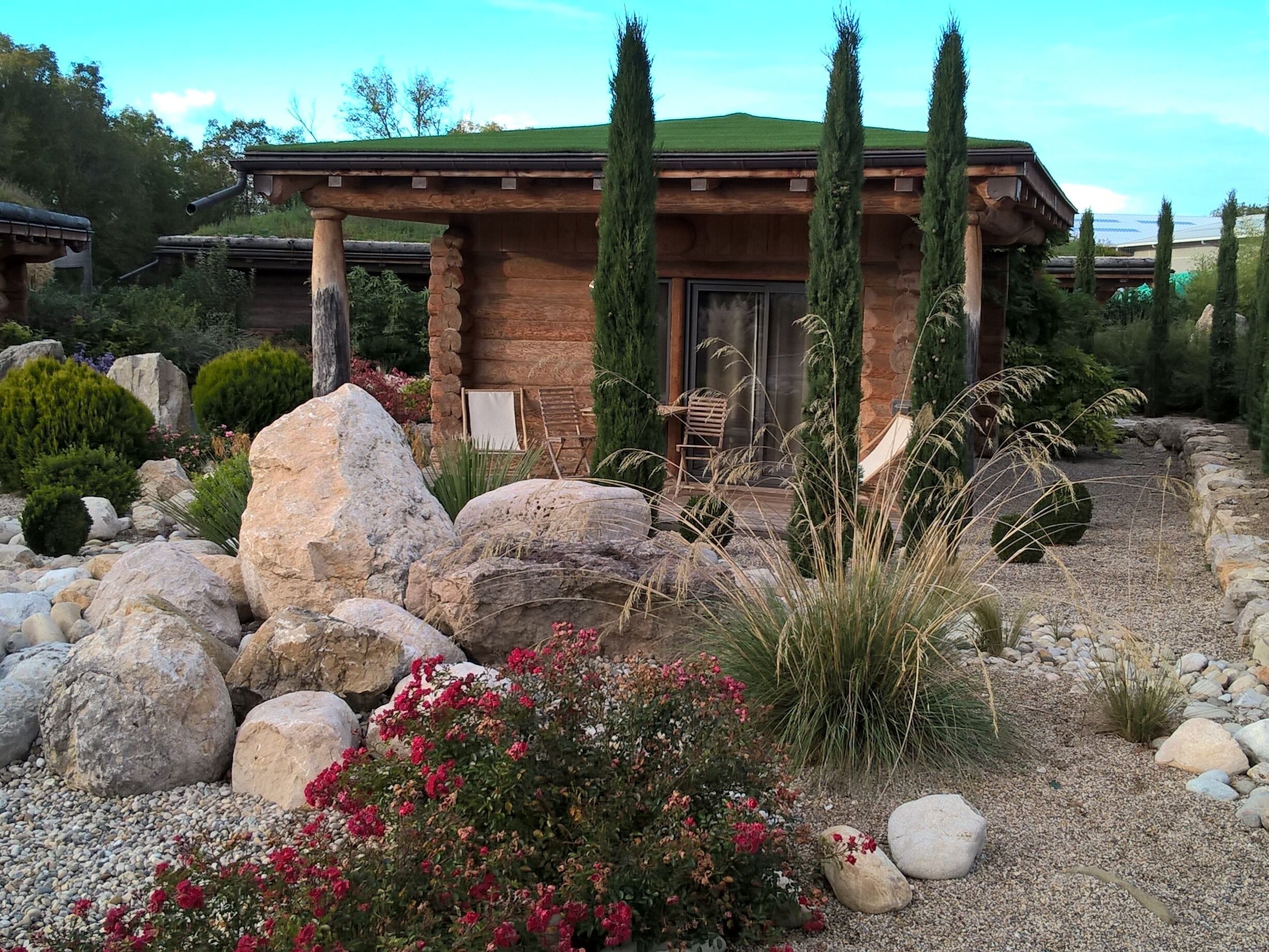A rustic cabin with a stone facade, a wooden deck, and a well-maintained garden with rocks and flowering plants.