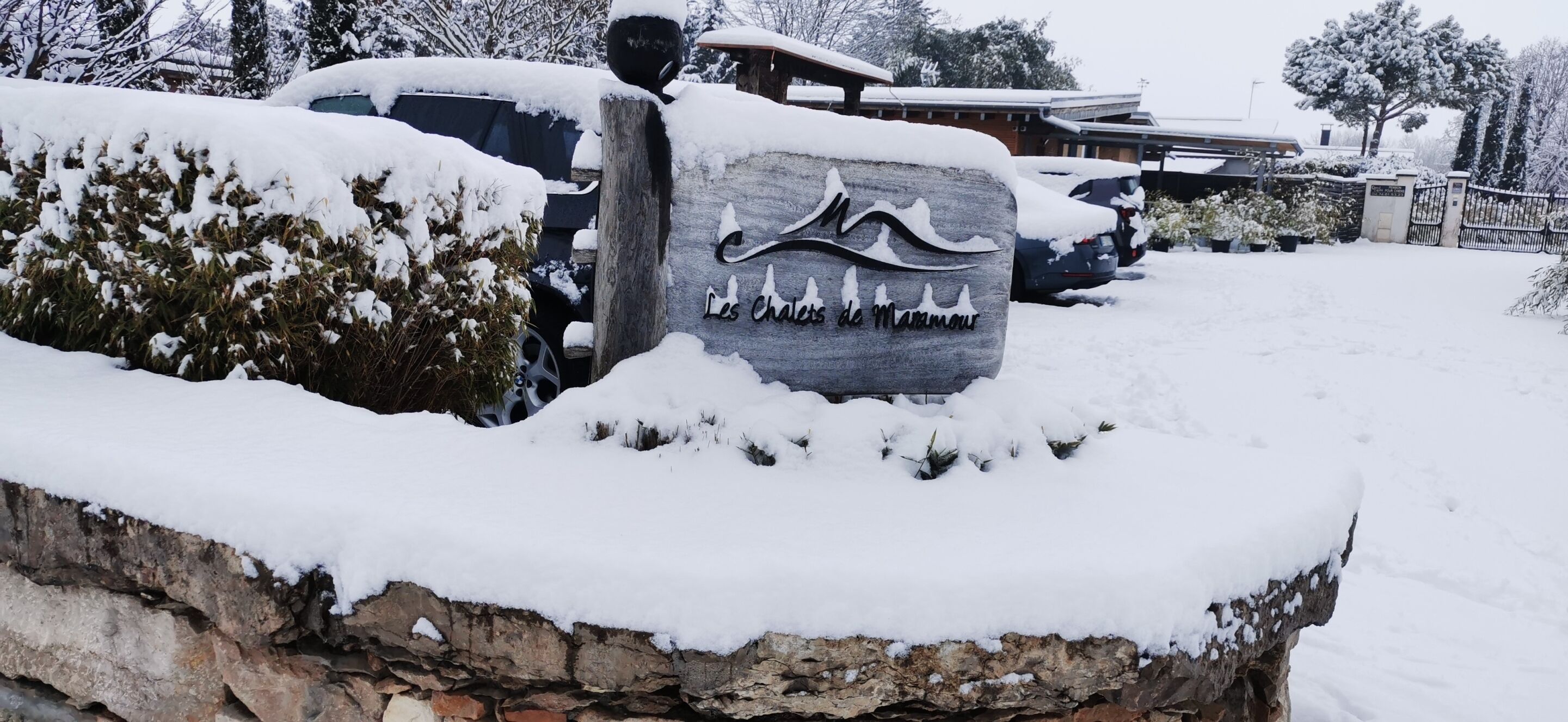 Un segnale di pietra ricoperto di neve con l'iscrizione "Les Cheneaux de Maromme" di fronte a un edificio.