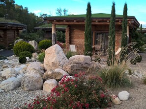 A rustic cabin with a stone facade, a green roof, and a well-maintained garden with rocks and flowering plants. - Les Chalets de Maramour (Chazey-sur-Ain)