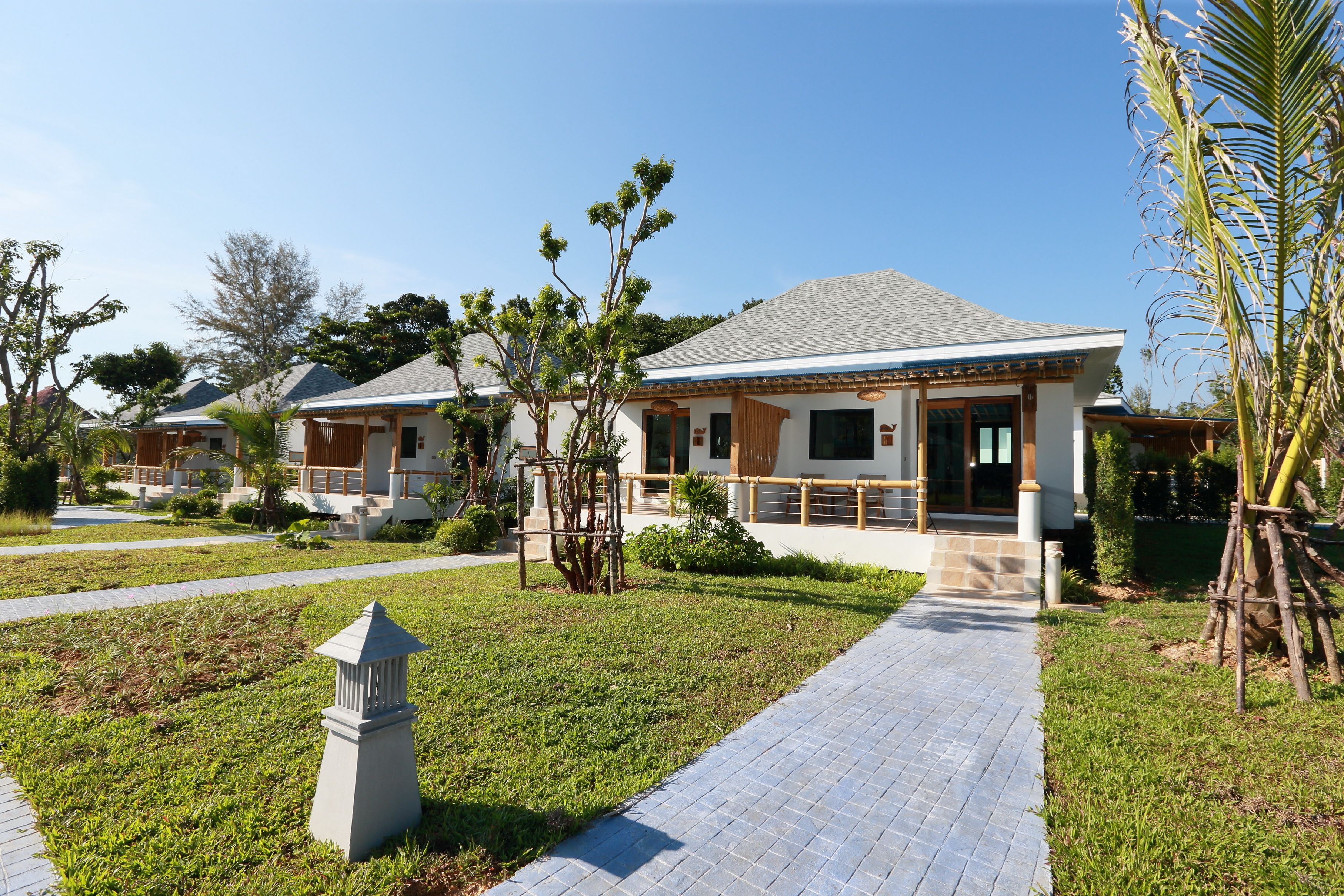 A modern hotel with a paved walkway, neatly trimmed grass, and a palm tree.