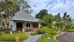 A bungalow with a tiled roof, surrounded by lush greenery and palm trees.