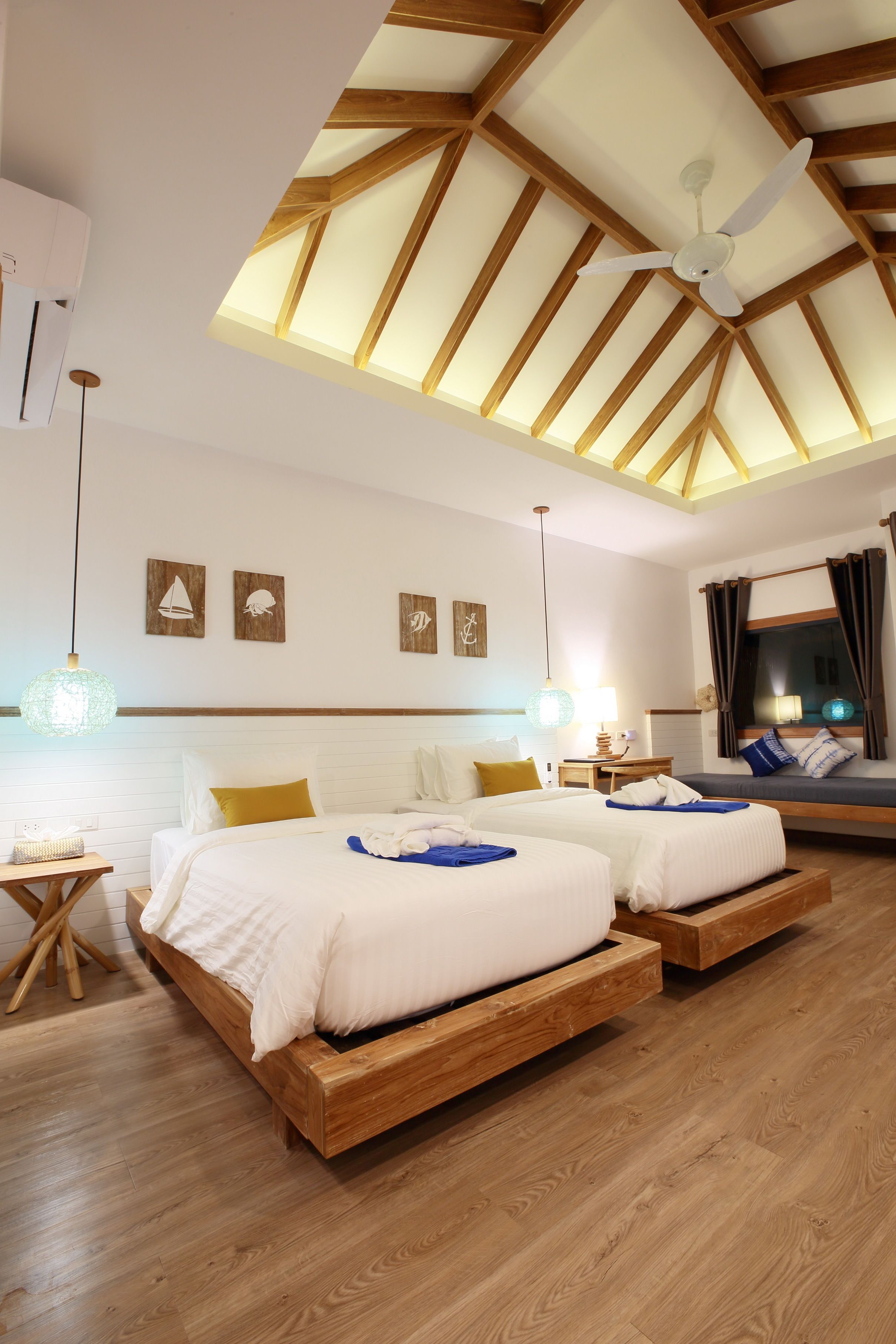 A modern hotel room with a high ceiling, wooden beams, two beds with white bedding, a skylight, and nautical-themed wall art.