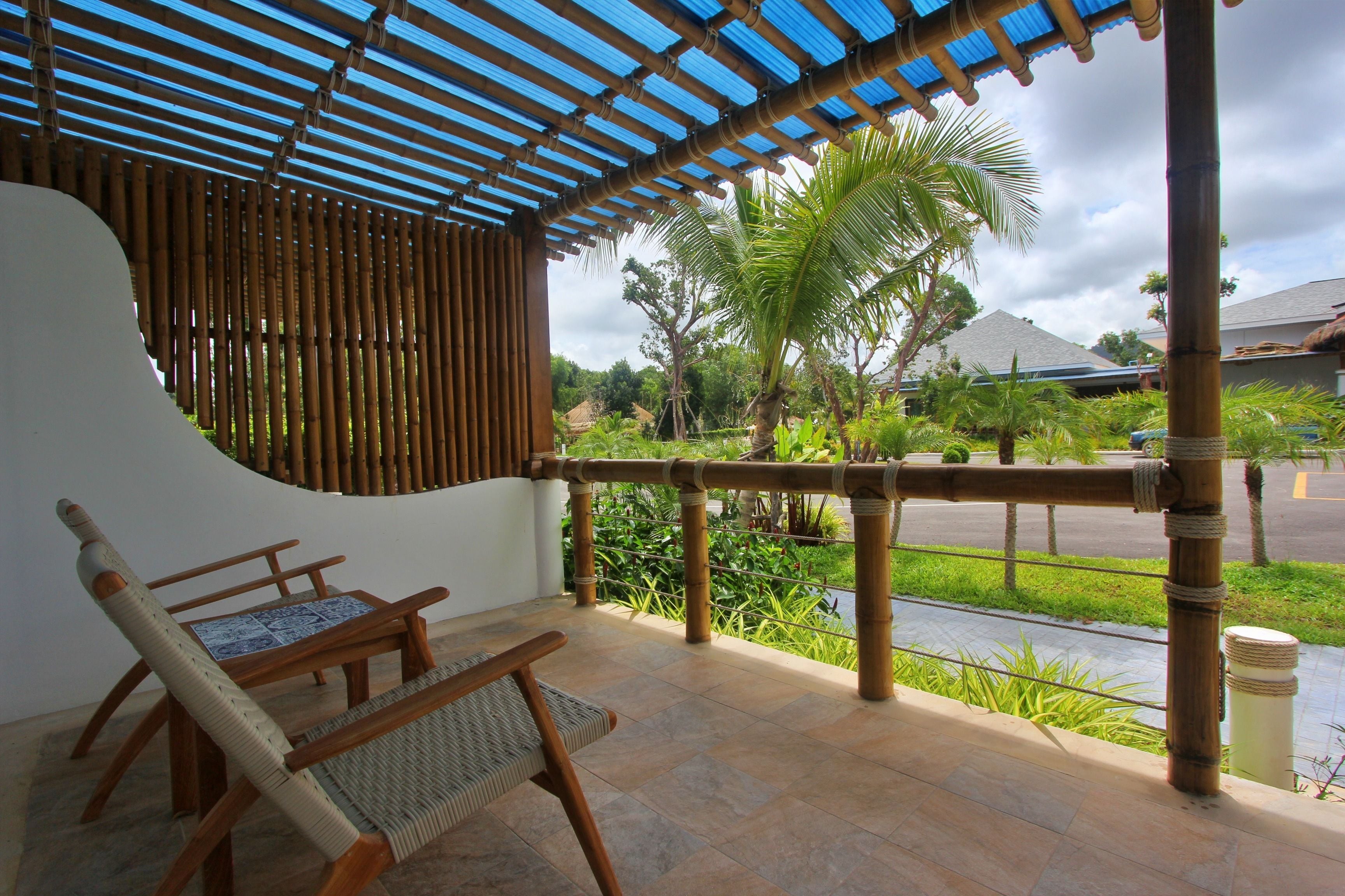 A covered outdoor seating area with bamboo railings, a view of the street, and a palm tree in the background.