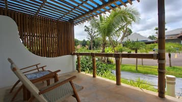 A covered outdoor seating area with bamboo railings, a view of the street, and a palm tree in the background.