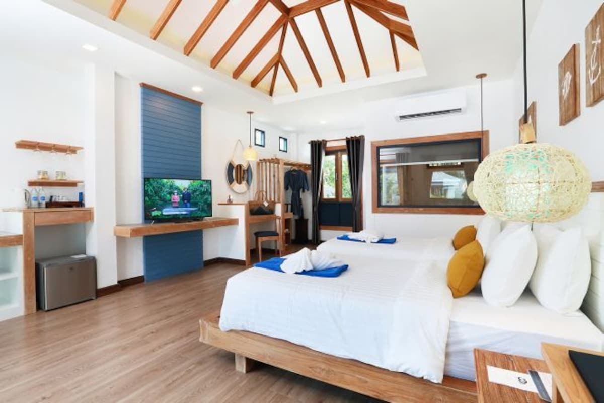 Une chambre d’hôtel moderne avec un plafond en bois, un grand lit avec une literie blanche, une télévision, un bureau avec une chaise et une grande fenêtre.