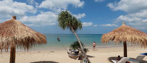A beach with thatched umbrellas and lounge chairs.