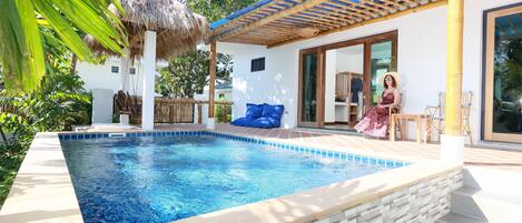 A swimming pool with a stone edge, a thatched roof, and a wooden deck.
