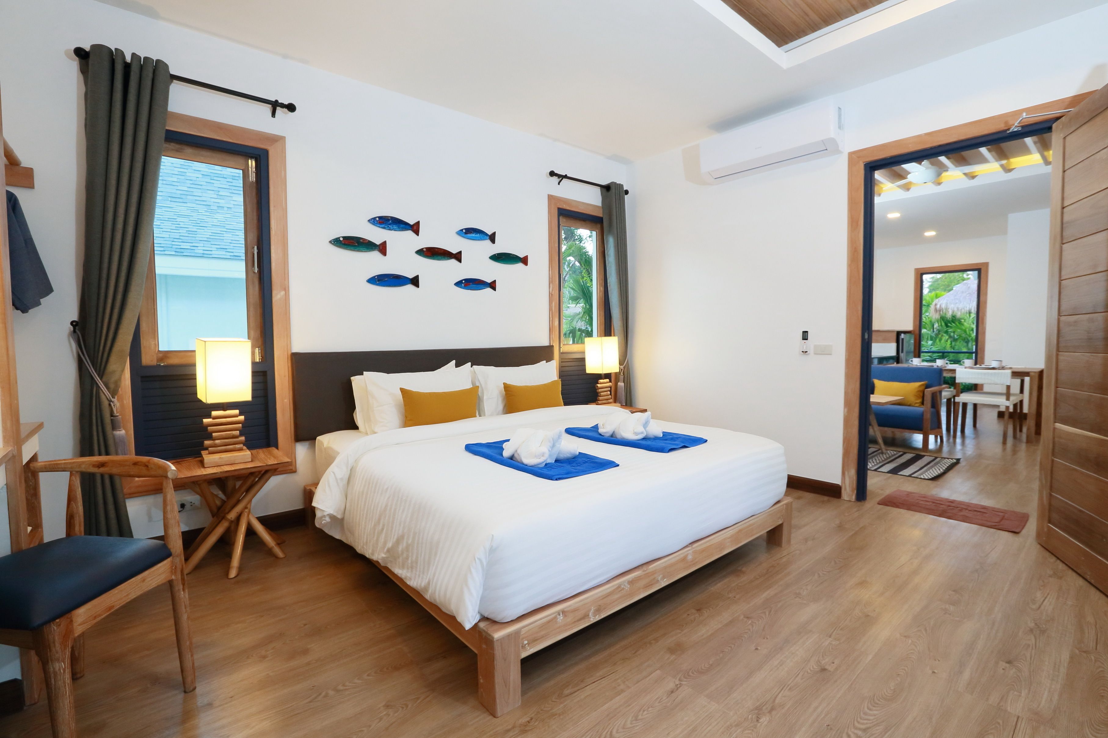 A hotel room with a wooden bed, a desk with a chair, a small table, and a window with curtains.