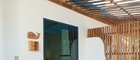 Un espacio de estar techado al aire libre con dos sillas de madera, una cesta colgante tejida y una señalización en la pared.