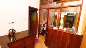 A compact room with a kitchenette, a wooden cabinet, and a window with curtains. - Yoho Milkyway Holiday Resort (Unawatuna)
