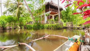 A boat with a thatched-roof structure on stilts, surrounded by lush greenery and a calm water body. - Yoho Milkyway Holiday Resort (Unawatuna)