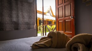 A room with a bed, a wooden door, and a view of a yellow building with a thatched roof. - Baan Kasirin Resort Pattaya Beach (Koh Lipe)