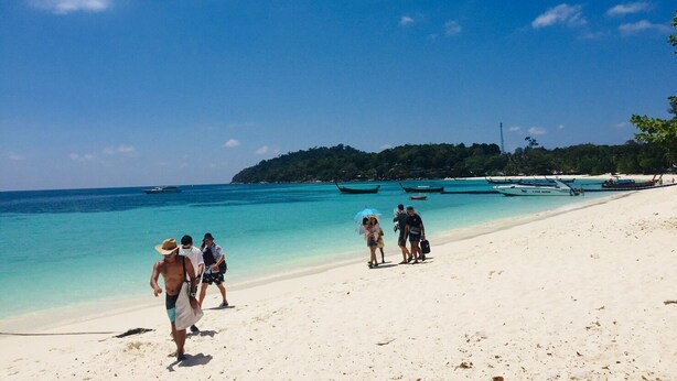 A beach with clear turquoise water, a sandy shore, and several boats in the background. - Baan Kasirin Resort Pattaya Beach (Koh Lipe)