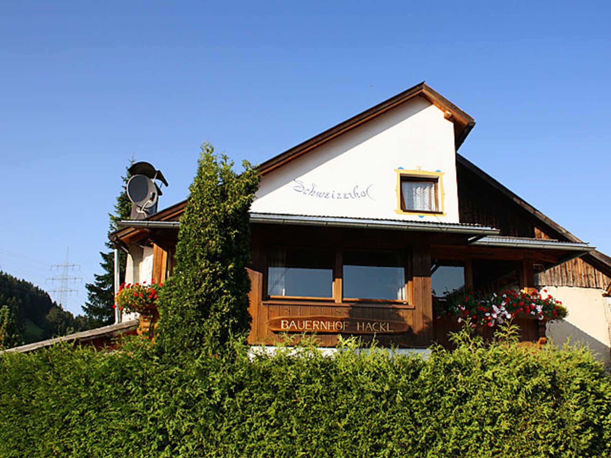 Ein traditionelles Chalet mit Holzfassade, einem Balkon voller Blumen und einem Schild mit der Aufschrift 'Baiernhof Hackl'.
