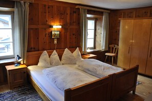 A wooden-paneled bedroom with a bed, bedside lamps, a nightstand, a chair, and a wardrobe. - Vacation apartment 1 - Schweizerhof (Wenns)