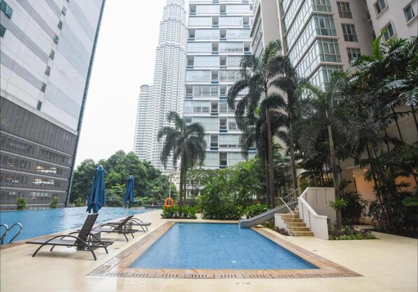 A swimming pool with lounge chairs and palm trees, surrounded by high-rise buildings.