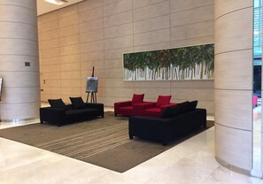 A lobby with two black sofas and a red sofa, a large painting of trees, and a sculpture on a pedestal.