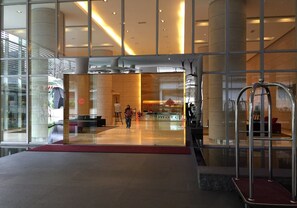 A modern hotel lobby with a glass facade, a central seating area, and a visible staircase.