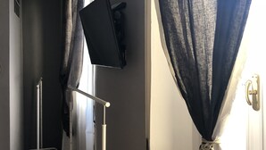 A hallway with a metal rack, a black television mounted on the wall, and a door with a rope tied around it. - Dimora Del Podestà (Castell'Arquato)