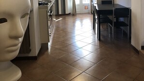 A hotel room with a tiled floor, a dining area with a table and chairs, a kitchen area, and a large window with curtains. - Dimora Del Podestà (Castell'Arquato)
