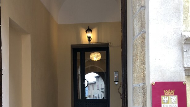 A staircase leading to a door with a light fixture above it. A sign with a crown and text is mounted on the wall to the right. - Dimora Del Podestà (Castell'Arquato)
