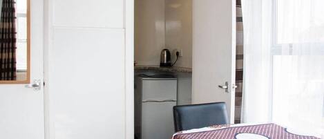 A compact room with a dining table, a kitchenette, and a window with curtains.