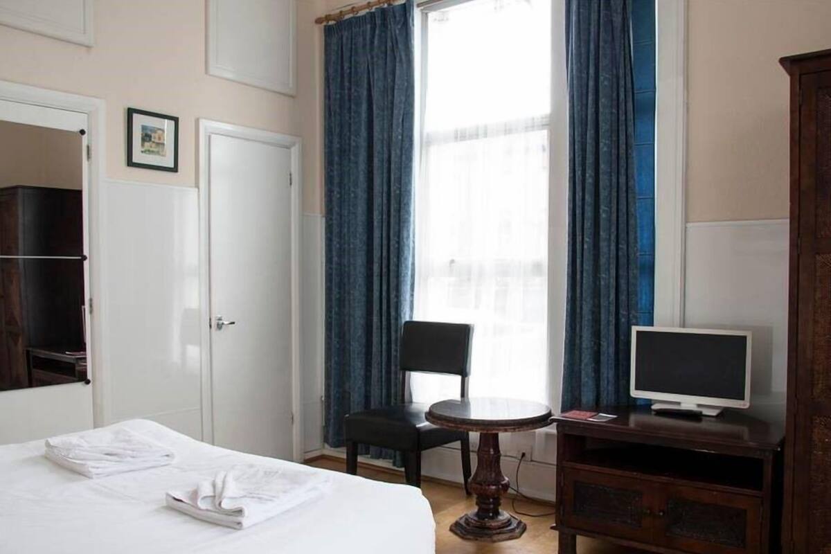A hotel room with a bed, a chair, a small table, a TV, and a wardrobe.