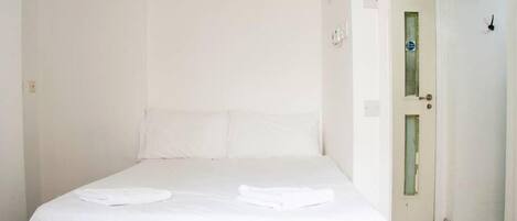 Ein sauberer, weißer Raum mit einem Einzelbett, einer Tür und einem Fliesenboden.