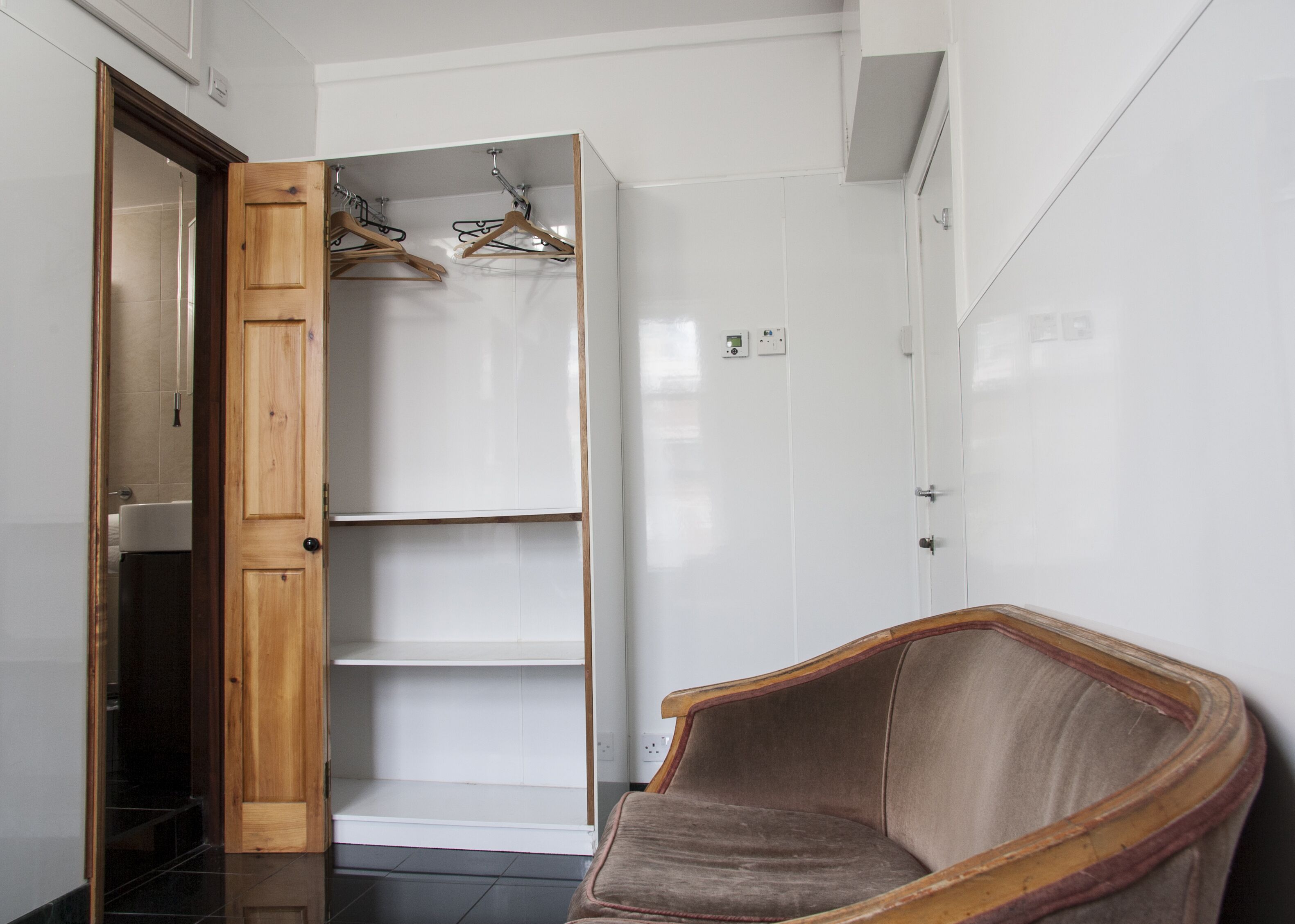 Une pièce avec une porte en bois, une chaise, une armoire blanche et une étagère avec des cintres.
