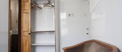 Une pièce avec une porte en bois, une chaise, une armoire blanche et une étagère avec des cintres.
